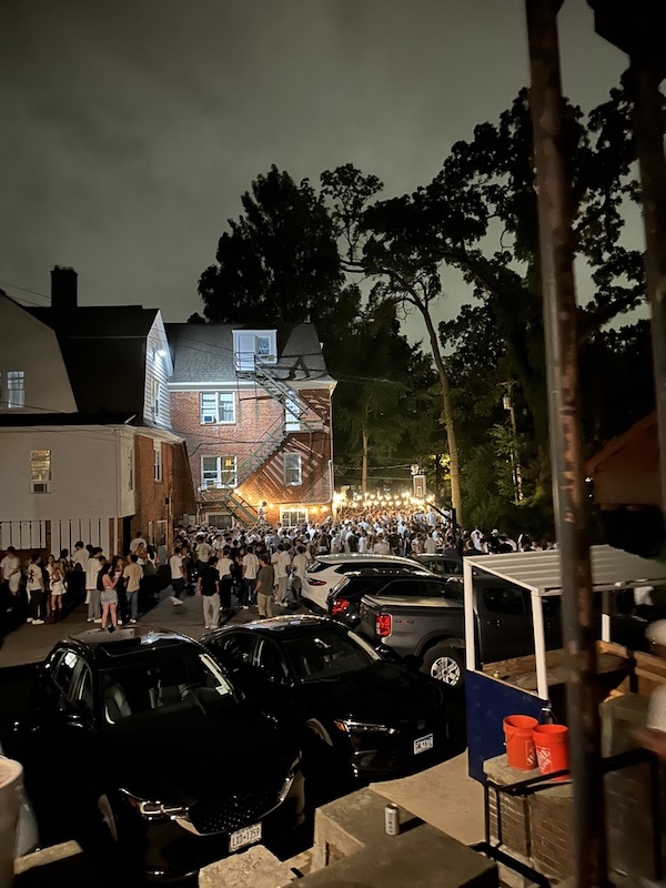 Multiple people gathered outside a house with a party going on at night
