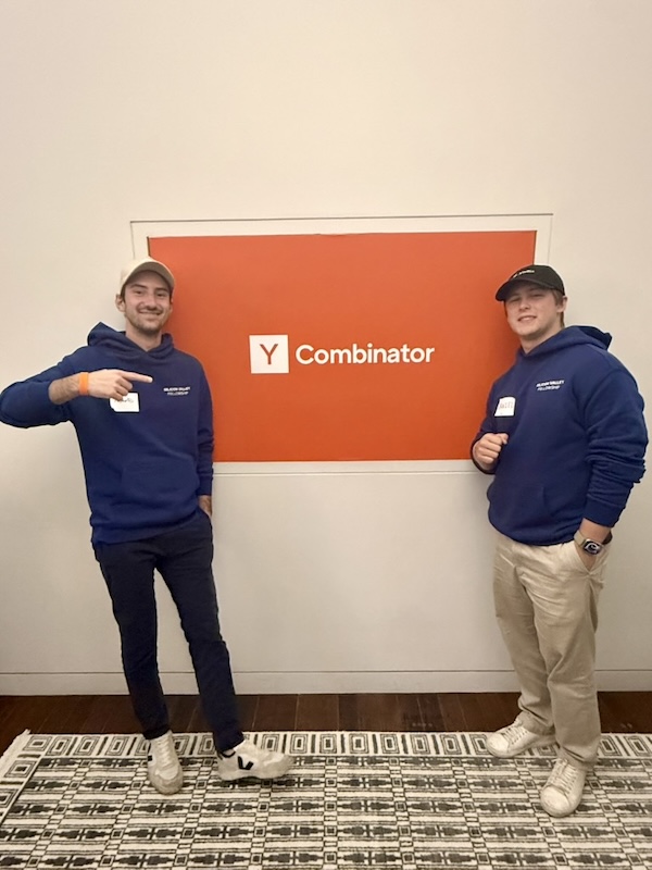 Two people standing in front of the Y Combinator sign